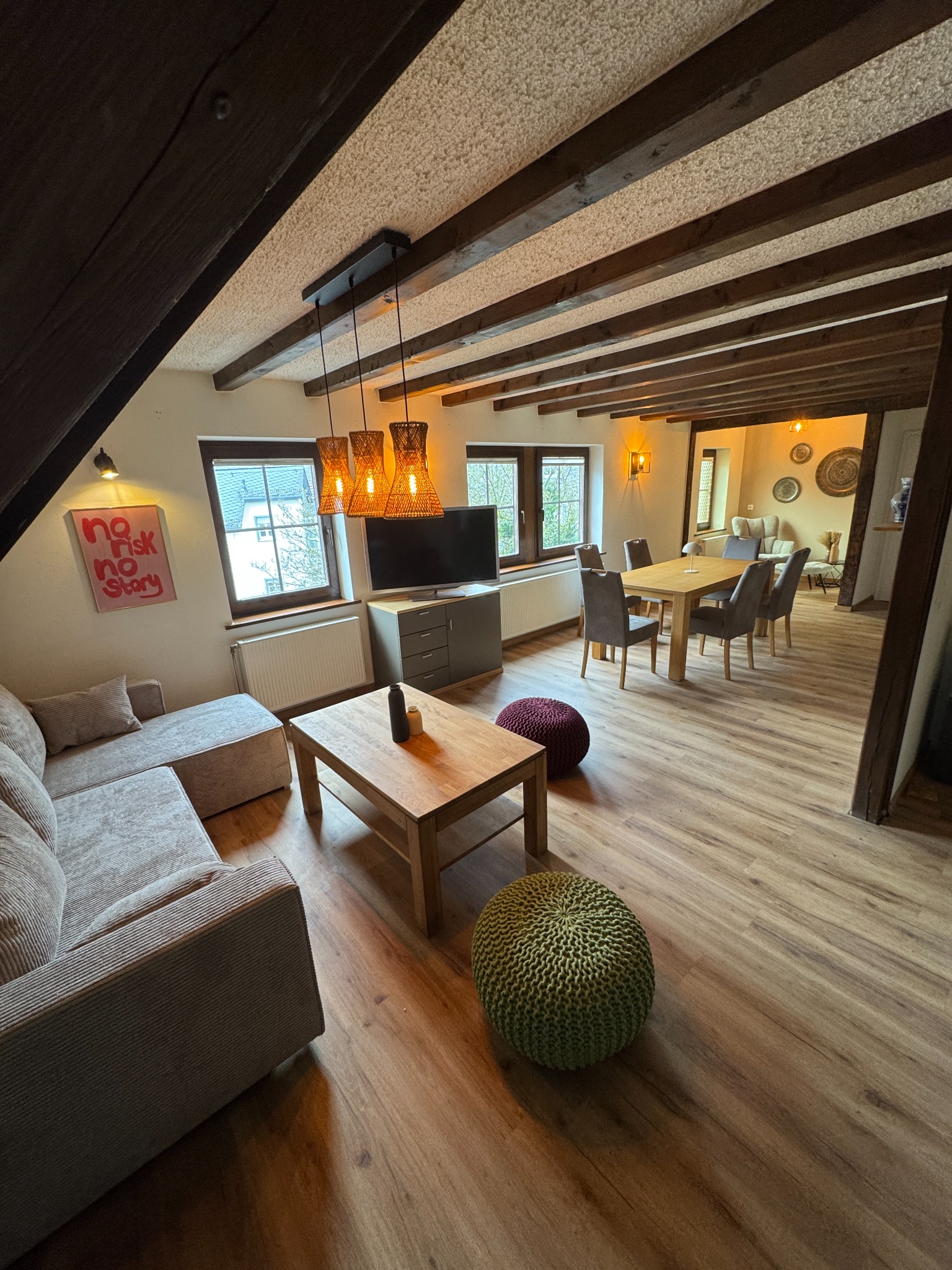 Wohn- und Essbereich von FACH.WERK mit Sofa, Couchtisch, Holzbalken und warmen Pendelleuchten